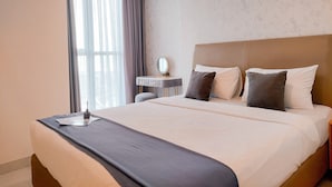 A hotel room with a large bed, a bedside table, a mirror, and a window with curtains. - Best Location 1BR Apartment at Gold Coast PIK (Jakarta)