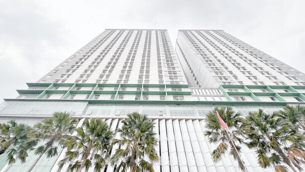 Un edificio de gran altura con diseño arquitectónico moderno, que presenta una cuadrícula de ventanas y un elemento estructural verde destacado en la base.