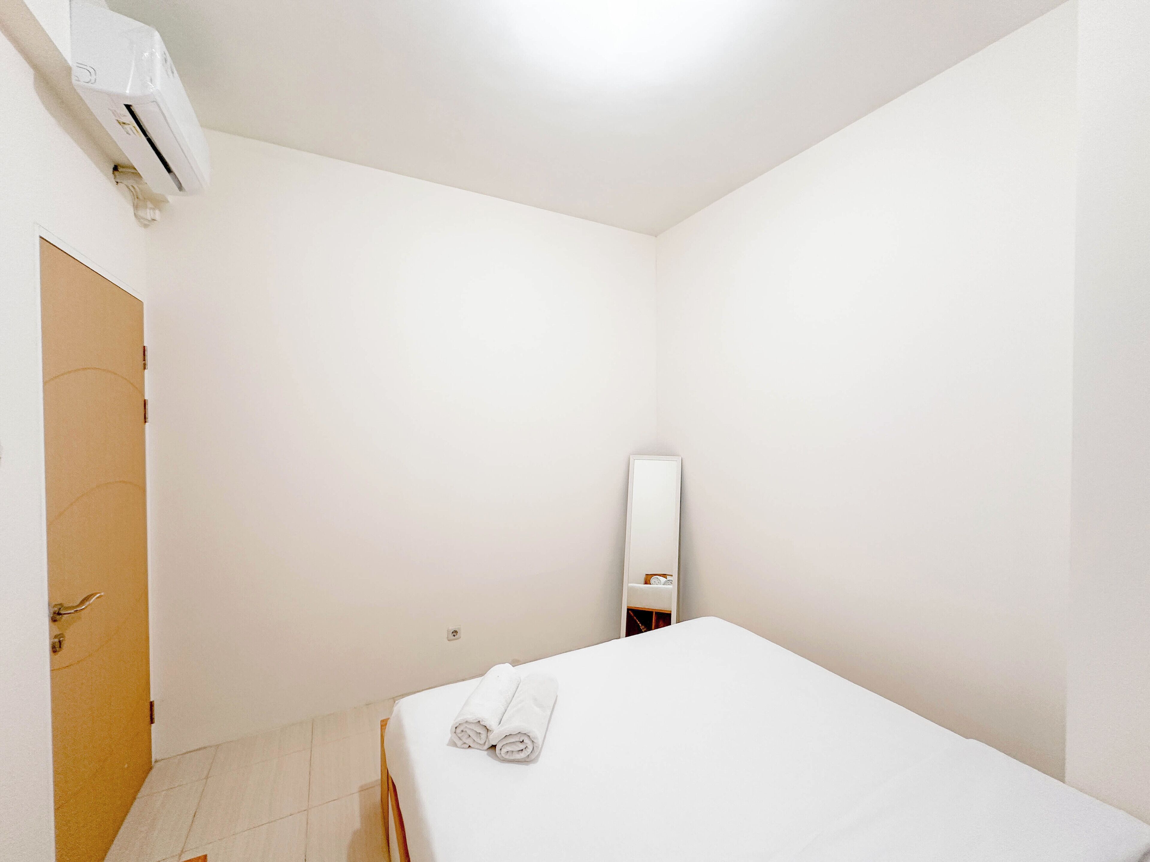 Et lille, rent værelse med en seng, en dør og en vægmonteret aircondition.