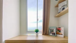 Un estudio con escritorio, una silla, ventanal con vistas, una planta y un libro en la estantería.