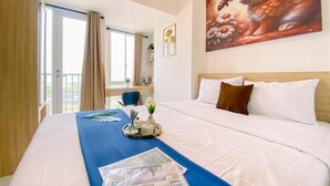 Habitación de hotel con una cama grande, una ventana con cortinas, un cuadro de un conejo y una bandeja con objetos sobre la cama.