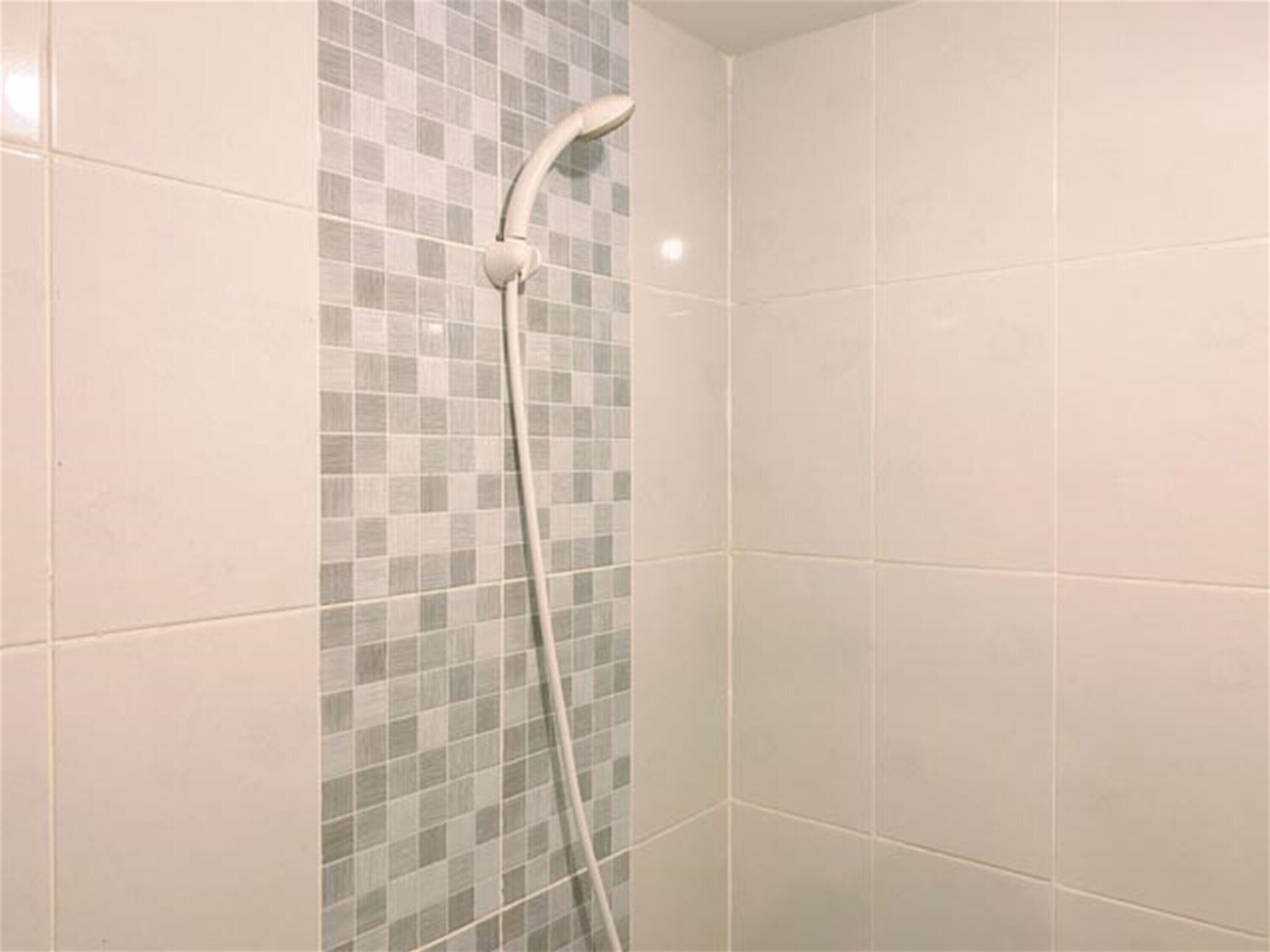 Eine Dusche mit einem weißen Schlauch und einer gefliesten Wand mit Schachbrettmuster.