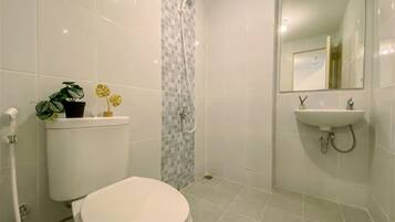 A bathroom with a toilet, a sink, a mirror, and a shower.