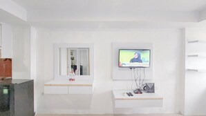 Una camera moderna e pulita con una televisione a muro, un tavolino con un telecomando e uno specchio sopra un lavandino.