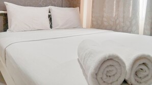 A neatly made bed with white linens, a pillow, and rolled towels. - The Urban 2BR at Vida View Makassar Apartment (Makassar)