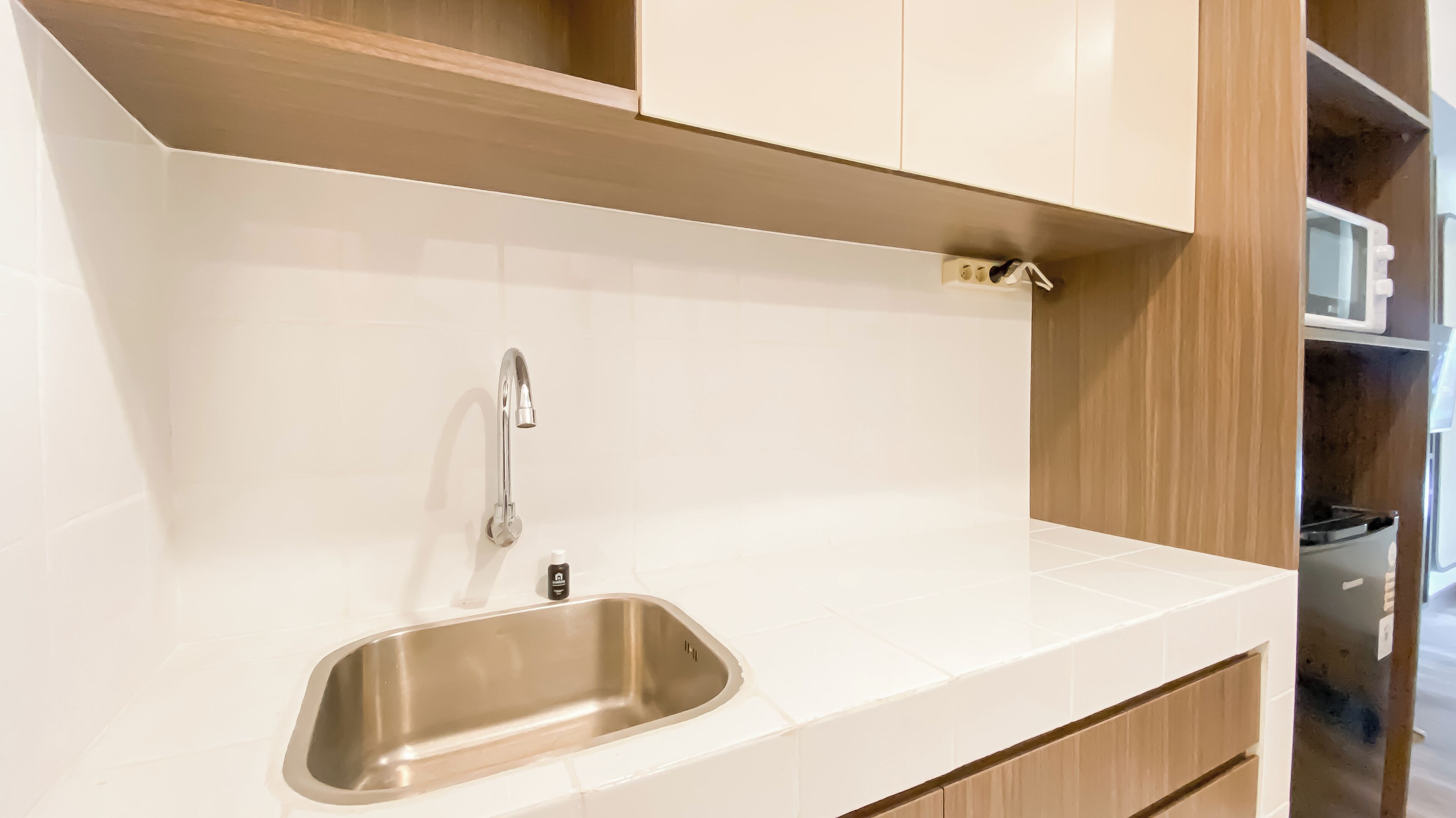 A modern kitchen with a stainless steel sink, white countertop, and wooden cabinetry.