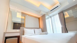 A modern hotel room with a large bed, a bedside table, an air conditioning unit, and a window with curtains. - The Bohemian 2BR at Tamansari La Grande Apartment (Bandung)