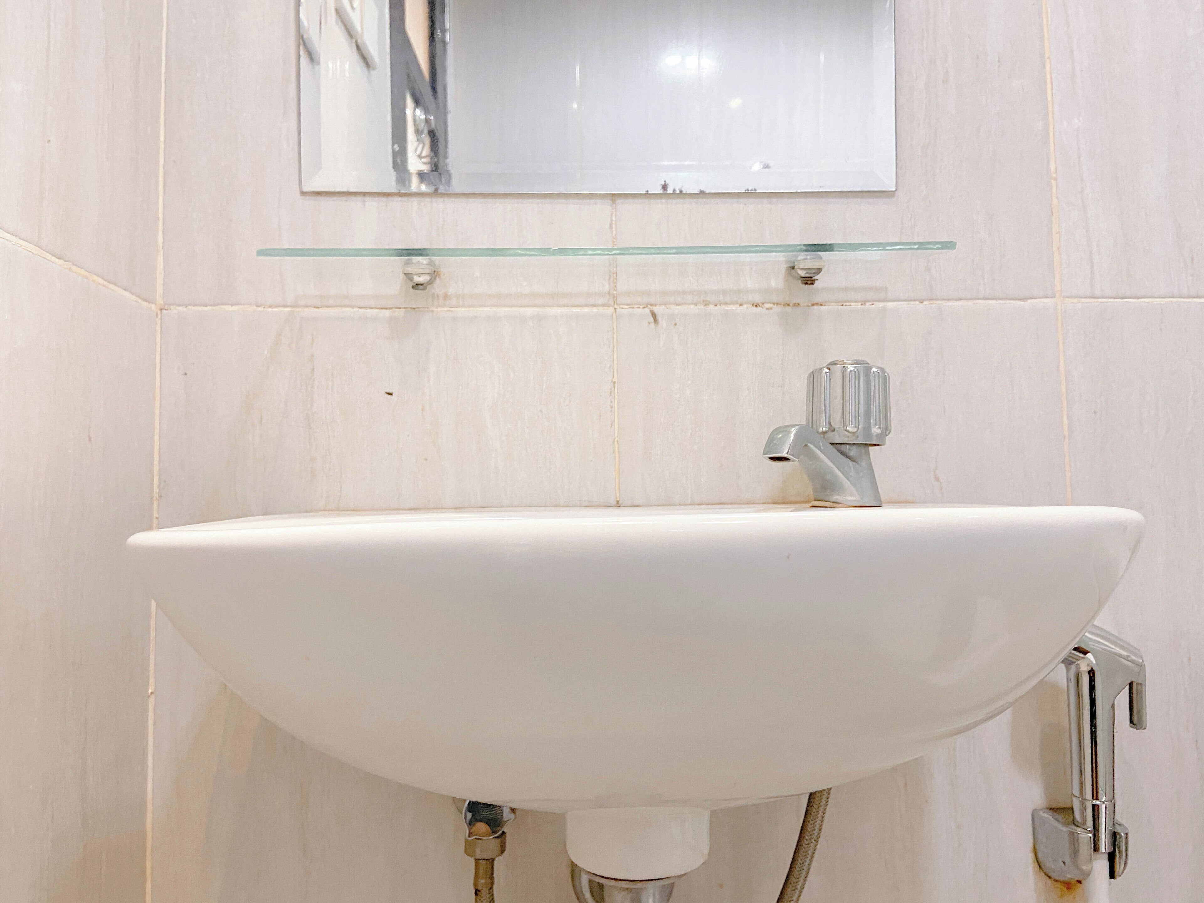 Ein Badezimmer mit einem weißen Waschbecken, einer Glasablage darüber und einem Spiegel.