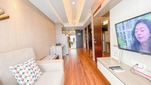 A modern hotel lobby with a sofa, a small table, and a TV screen displaying a person. - The Bohemian 2BR at Tamansari La Grande Apartment (Bandung)