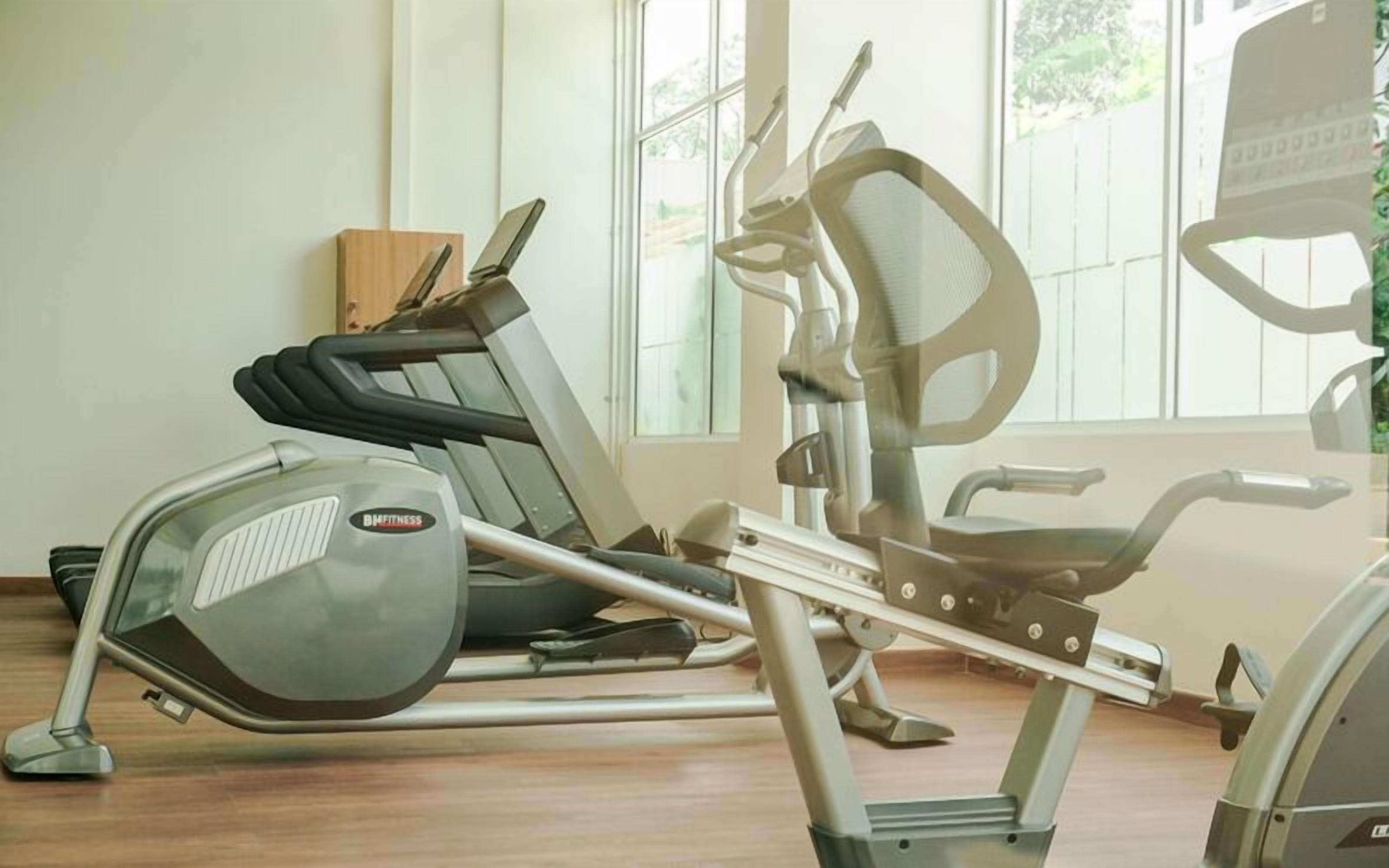 A gym with exercise equipment, including a treadmill and a stationary bike, with a window providing natural light.