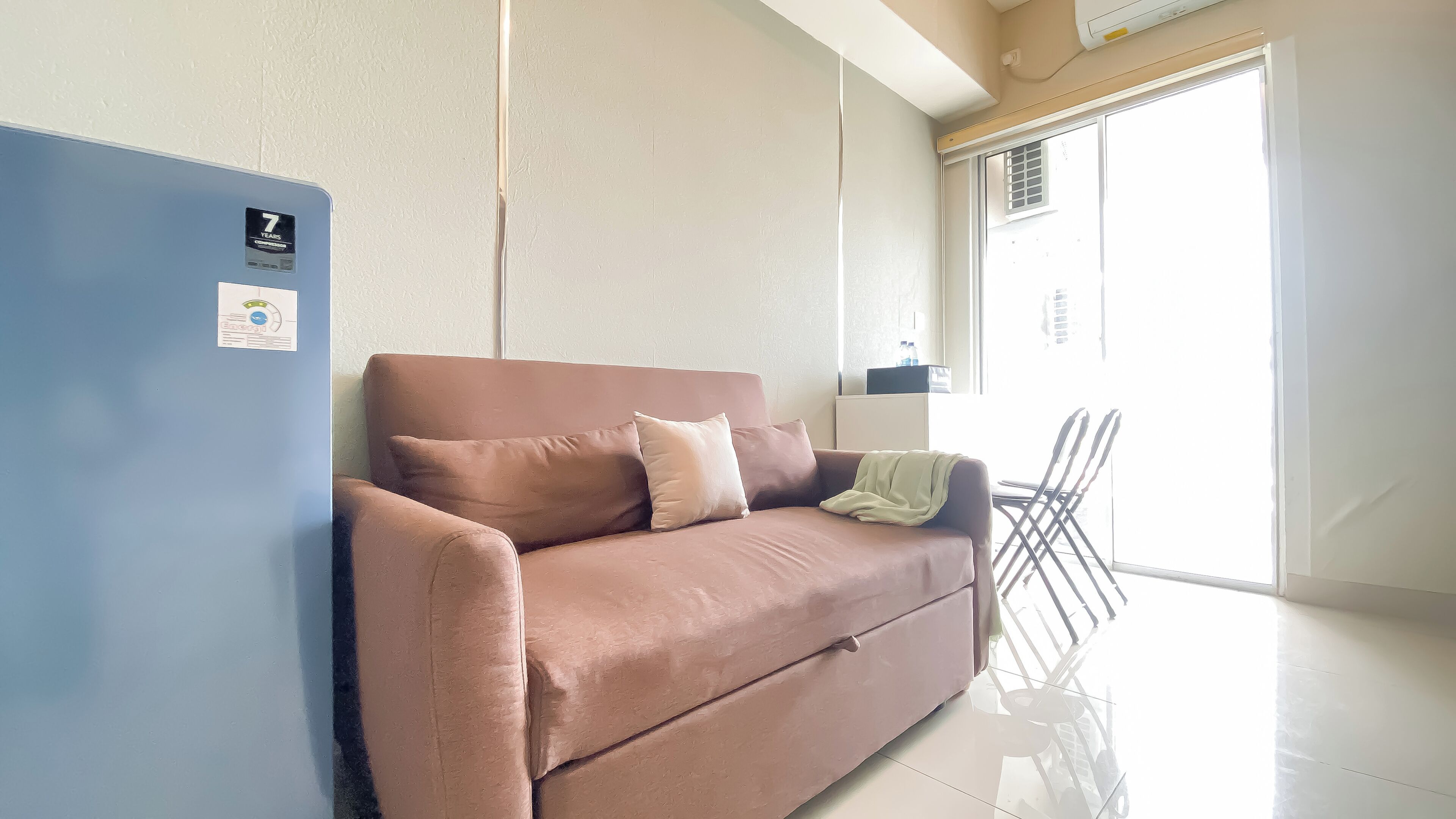 A living room with a brown sofa, a blue wall, and a window with a view of the outside.