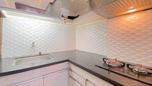 A modern kitchen with a stainless steel sink, black countertop, and gas stove. - The Urban Style 2BR at Suites @Metro Apartment (Bandung)