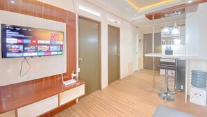 A modern hotel room with a wooden floor, a flat-screen TV mounted on the wall, a small bar area with a stool, and a water dispenser. - The Urban Style 2BR at Suites @Metro Apartment (Bandung)