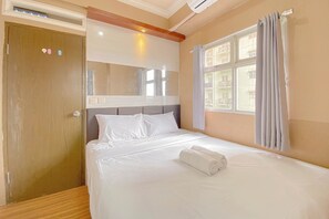 Una camera d'hotel con un letto grande, una porta in legno, una finestra con tende e uno specchio sopra il letto.