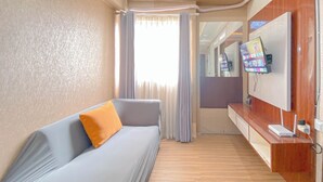 A hotel room with a grey sofa, a wooden console table, a flat-screen TV, and a large window with curtains. - The Urban Style 2BR at Suites @Metro Apartment (Bandung)