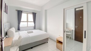 A modern bedroom with a bed, a desk, a chair, a window with curtains, and a sliding glass door leading to a balcony.