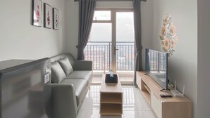 Una sala moderna con un sofá gris, una mesa de centro de madera y un televisor sobre un mueble de madera. Se ve un balcón con barandilla a través de la ventana.