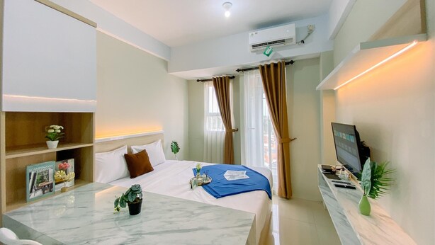 Camera d'albergo moderna con un letto, una scrivania con un computer, una TV e una piccola pianta.