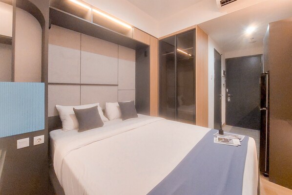 A modern hotel room with a large bed, built-in wardrobe, and a glass shower enclosure.