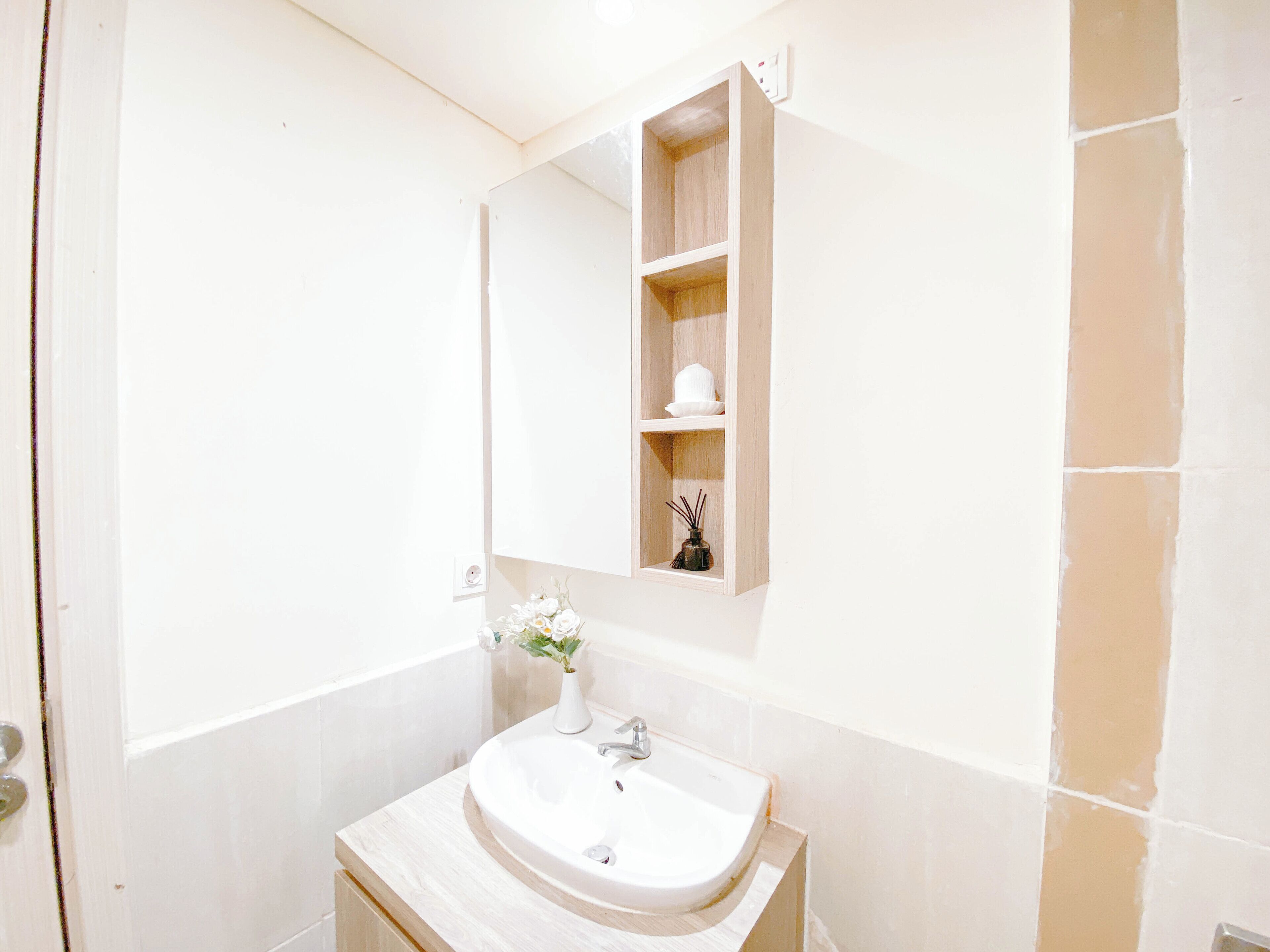 Un baño con un lavabo blanco, un espejo y un pequeño estante con un florero.