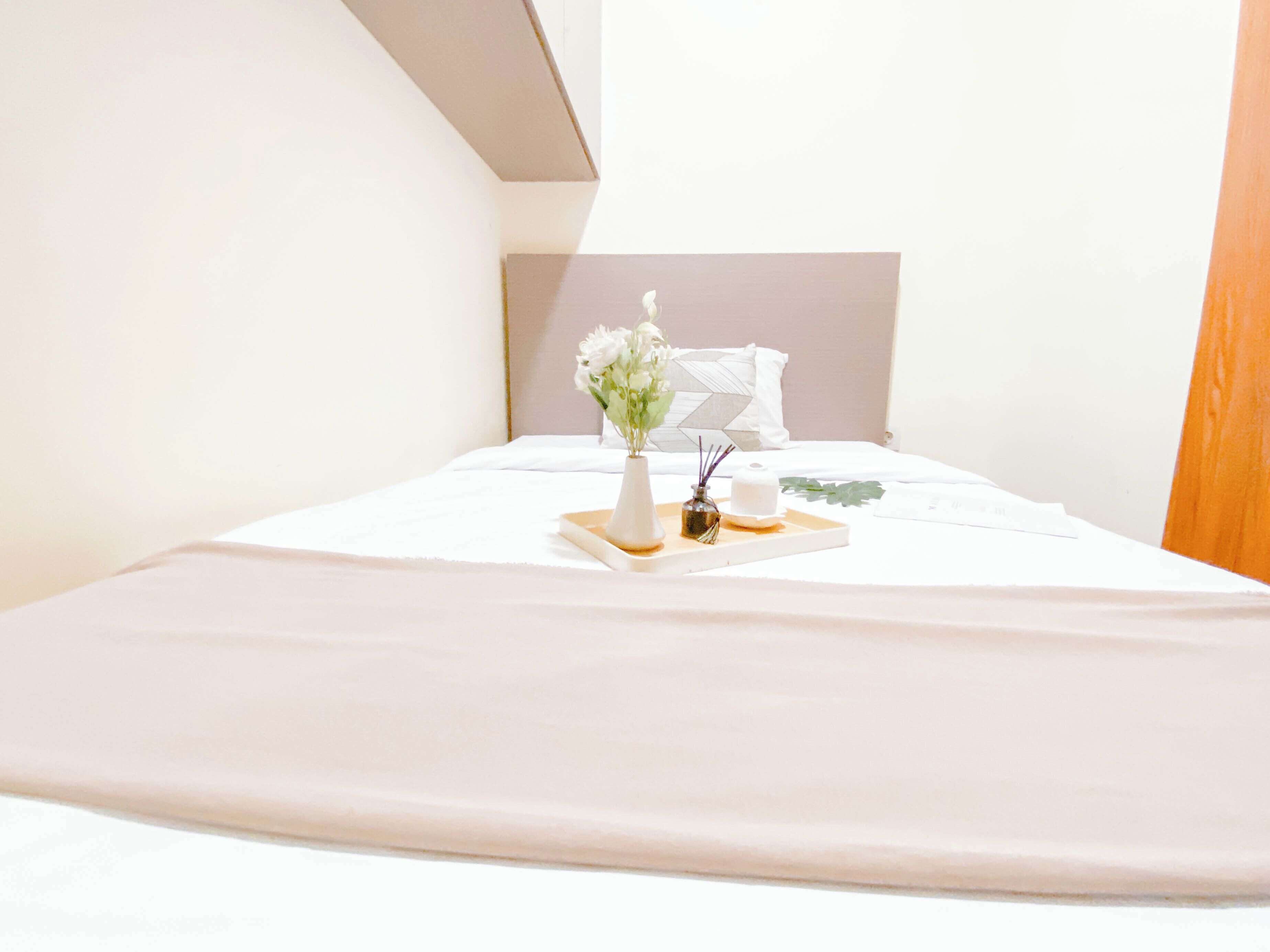 A neatly made bed with a white headboard, a tray with a vase of flowers, and a small candle.