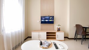 A hotel room with a TV mounted on the wall, a small table with a tray, a remote control, and a chair. - New Furnished and Homey 2BR Apartment Nifarro Park (Jakarta)