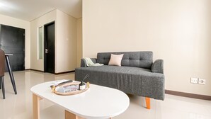 A living room with a grey sofa, a white coffee table, and a black door. - New Furnished and Homey 2BR Apartment Nifarro Park (Jakarta)