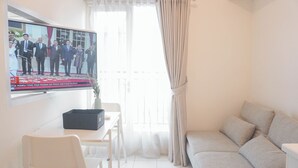 A living room with a TV displaying a group of people, a sofa, a table with a black box, and a chair.