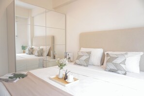 Ein modernes Schlafzimmer mit einem großen Spiegel, einem Bett mit weißer Bettwäsche und einem Nachttisch mit einer Blumenvase.