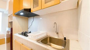 A kitchen with a stainless steel sink, a gas stove, and wooden cabinets. - Cozy Style Studio Apartment at Tokyo Riverside PIK 2 (Teluknaga)