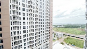 A high-rise residential building with multiple balconies and a view of a green landscape and water body. - Cozy Style Studio Apartment at Tokyo Riverside PIK 2 (Teluknaga)