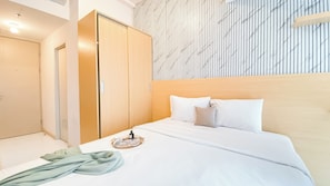 A hotel room with a bed, a bedside table, a mirror, a wardrobe, and a striped wall pattern.