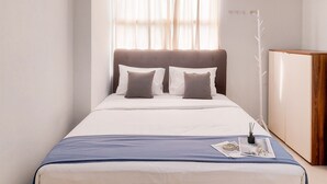 A neatly made bed with a blue bedspread, two pillows, and a small table with a magazine and a candle. - Nice and Comfy 2BR Apartment At Silkwood Residence (Tangerang)