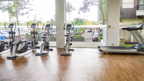 A gym with exercise equipment and a view of parked cars and greenery outside. - Nice and Comfy 2BR Apartment At Silkwood Residence (Tangerang)