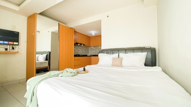 A bedroom with a bed, a TV, a wardrobe, and a kitchen area. - Cozy and Best Deal Studio Apartment Amethyst (Jakarta)