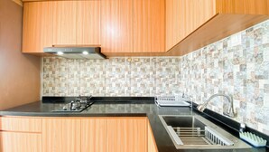 A kitchen with wooden cabinets, a gas stove, a sink, and a tiled backsplash. - Cozy and Best Deal Studio Apartment Amethyst (Jakarta)