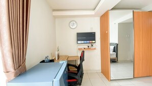 A room with a desk, chair, TV, clock, and a door leading to another room. - Cozy and Best Deal Studio Apartment Amethyst (Jakarta)