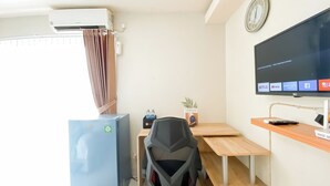 A hotel room with a desk, a chair, a TV mounted on the wall, an air conditioner, and a window with curtains. - Cozy and Best Deal Studio Apartment Amethyst (Jakarta)