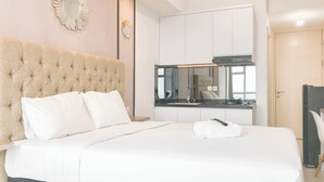 A neatly made bed with white linens, a tufted headboard, and a mirror above it.