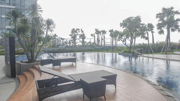 A pool area with lounge chairs and a view of palm trees and a building in the background.