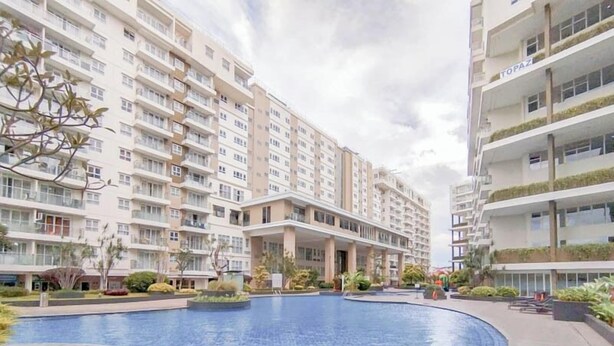 Un moderno edificio de apartamentos con piscina en un patio central, rodeado de vegetación y otros edificios residenciales.