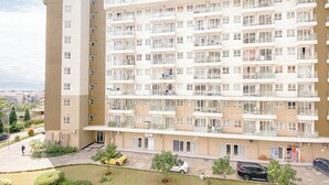 Un edificio residencial de varios pisos con balcones, zona de estacionamiento y un pequeño jardín.