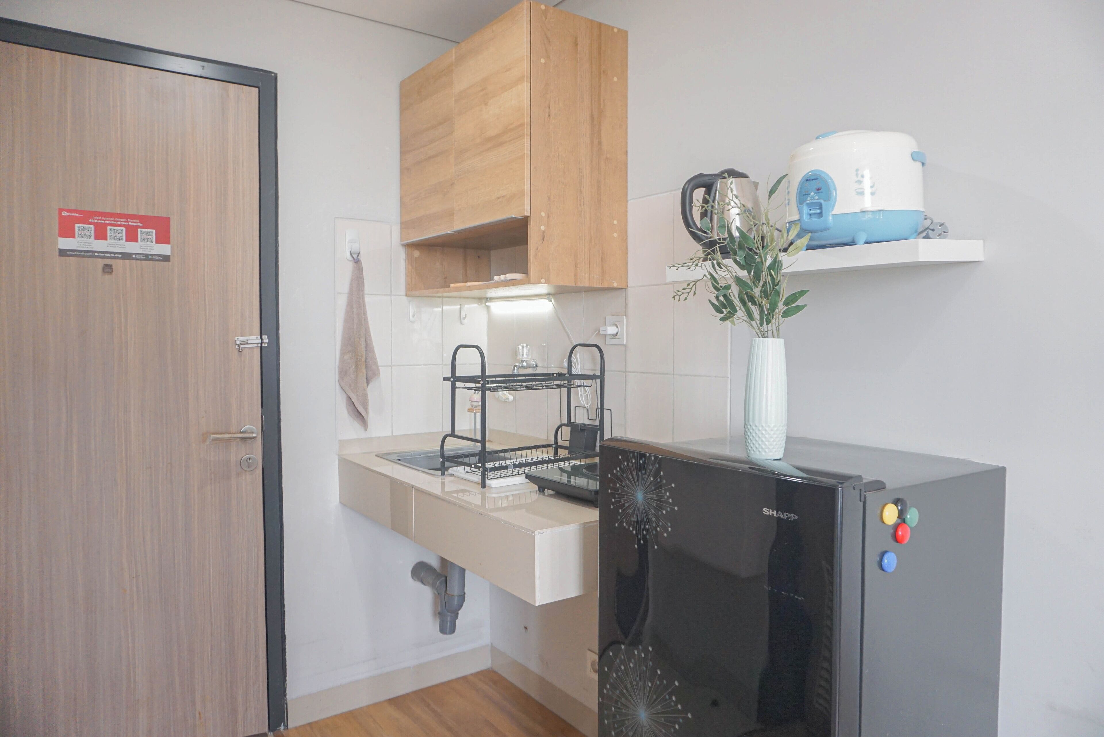 Een keuken met een houten kast, een spoelbak, een zwarte koelkast en een koffiezetapparaat op een plank.