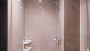 A shower area with a glass door, a handheld showerhead, and a wall-mounted faucet. - Spacious and Homey Studio Room Paramount Skyline Apartment (Gading Serpong)