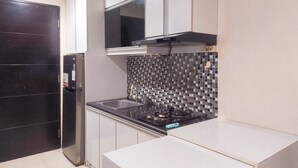 A compact kitchen with a black refrigerator, a tiled backsplash, and white cabinetry. - Spacious and Homey Studio Room Paramount Skyline Apartment (Gading Serpong)