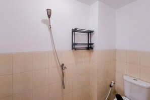 A bathroom with beige tiles, a toilet, a shower with a handheld showerhead, and a black towel rack. - Comfy Studio Apartment at Urbantown Serpong (South Tangerang)