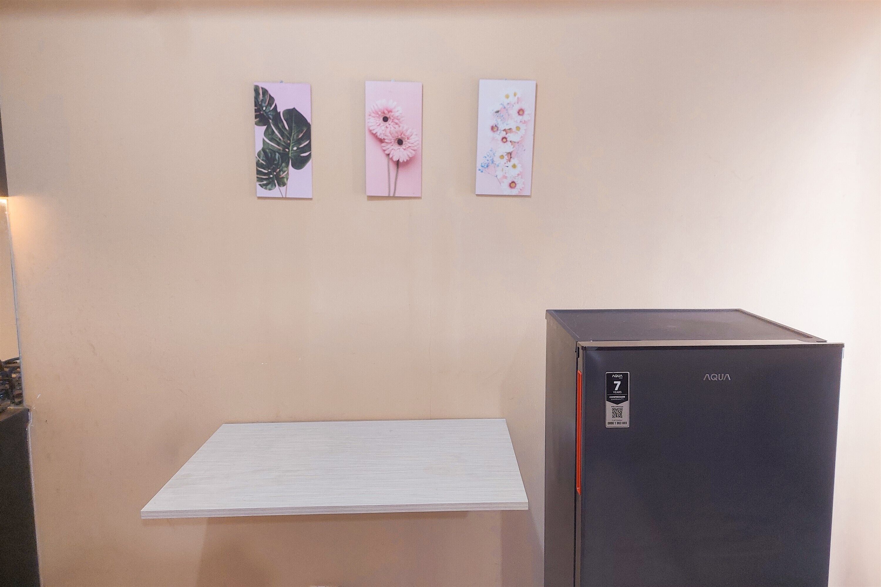 A room with a beige wall, a black refrigerator, and three framed pictures.