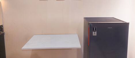 A room with a beige wall, a black refrigerator, and three framed pictures.
