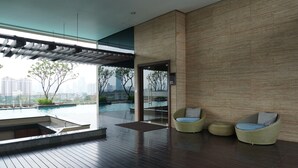 A modern indoor pool area with wooden flooring, two wicker chairs, and a glass door leading outside. - Elegant and Spacious Studio at Kemang Mansion Apartment (Jakarta)