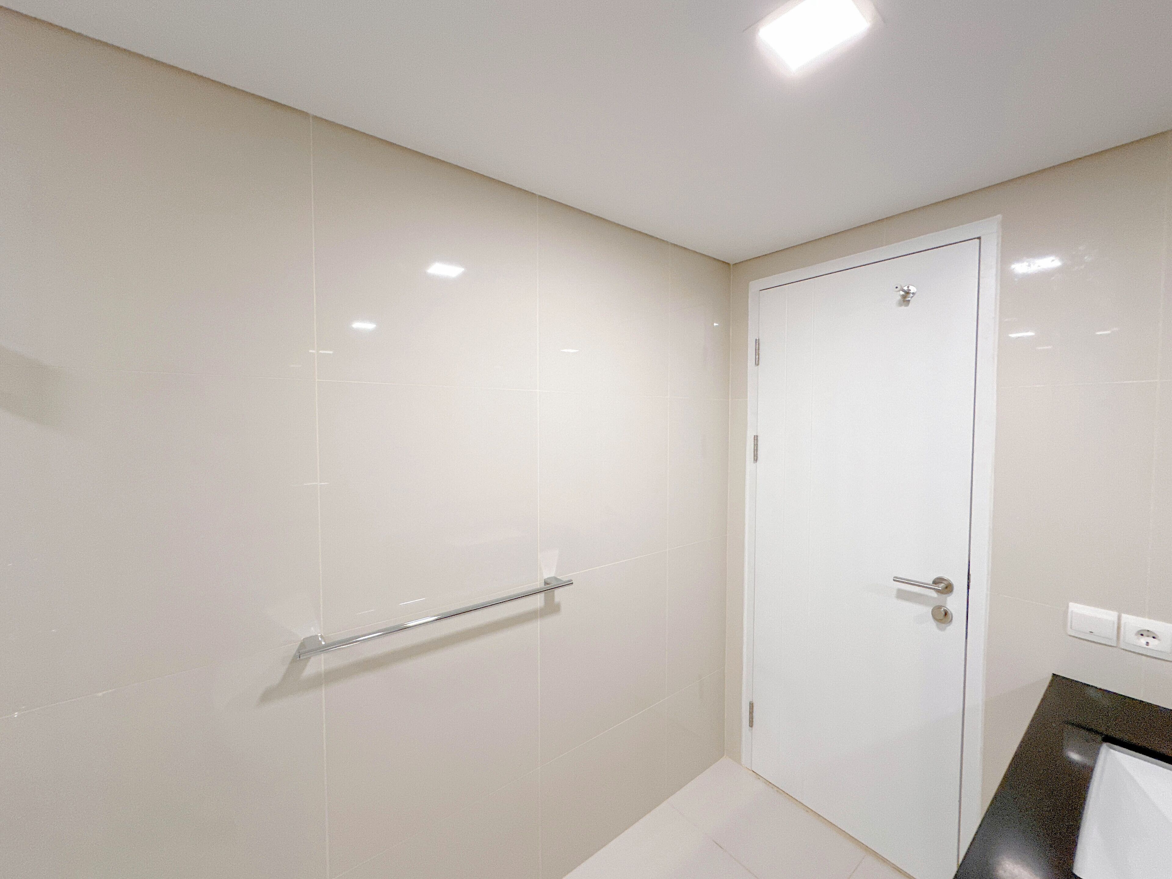 A bathroom with white tiles, a glass shower enclosure, a white door, and a towel rack.